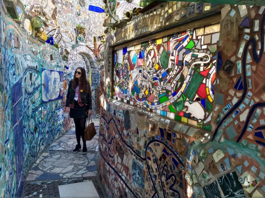 A woman stands admiring the art around her. She is in a colorful maze full of glittering mosaics. Colorful tiles are placed throughout.