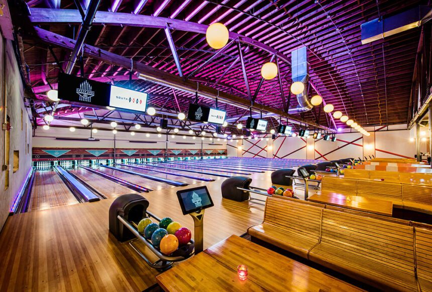 Bright purple lights shine down on bowling lanes and bowling balls in an open space