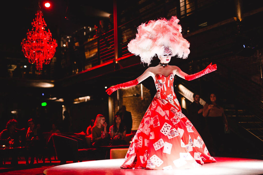 A performer in a red gown and giant white wig performs at a dinner theater.