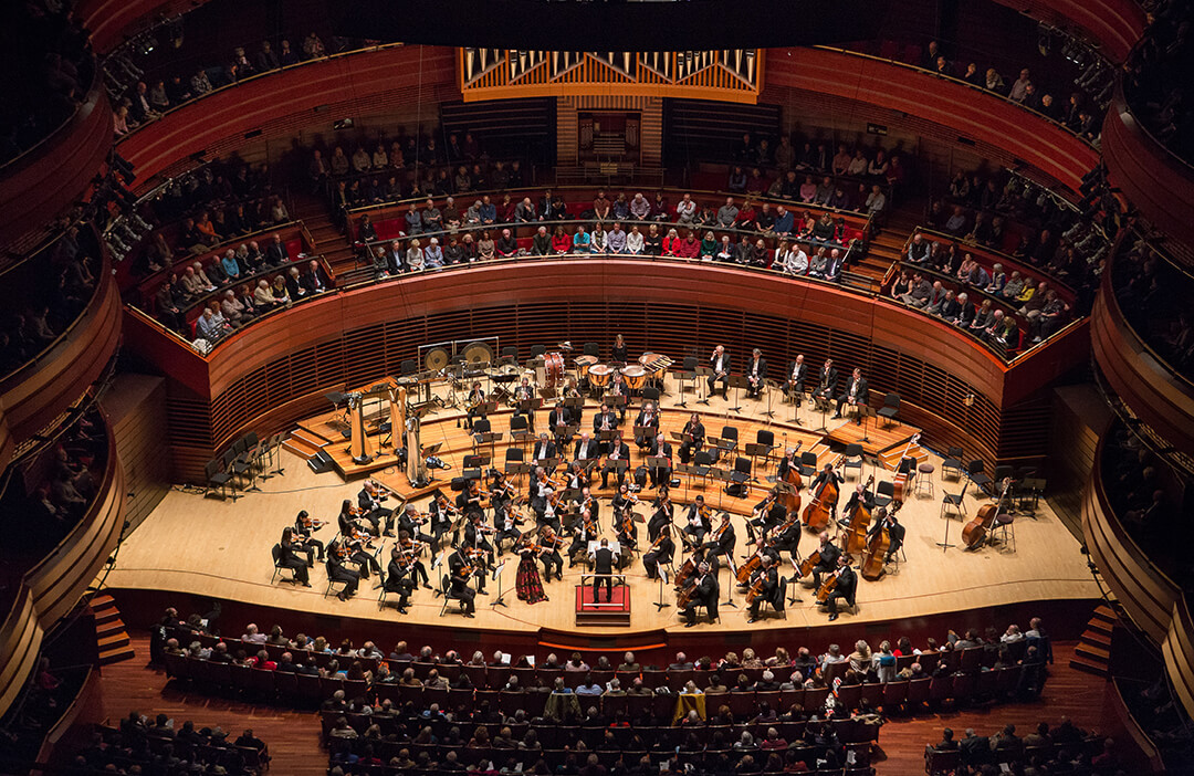 An overhead view of an orchestra playing on stage to a full audience.