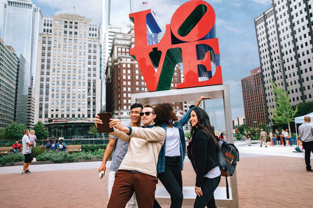 A group of young people gather in front of the LOVE Sculpture to snap a selfie