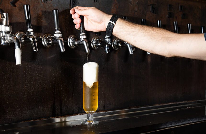 A person pours a beer from the tap.