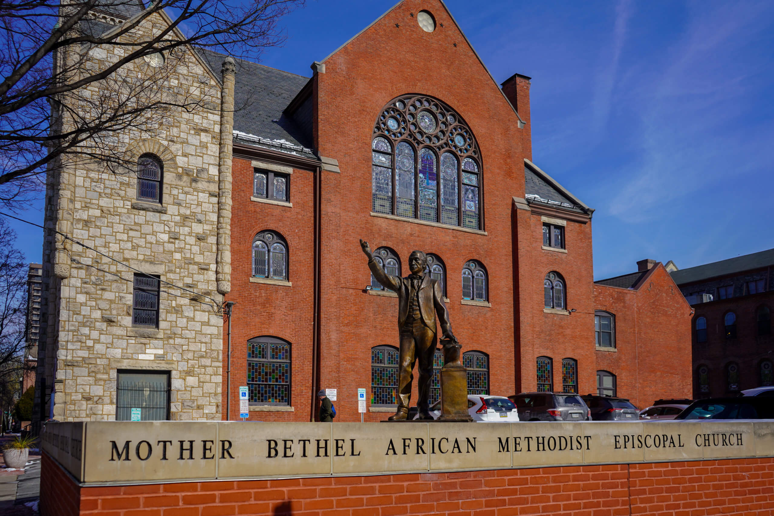 A brick wall in front of a brick building, a statue is in the middle. across the front reads Mother Bethel African Methodist Episcopal Church.