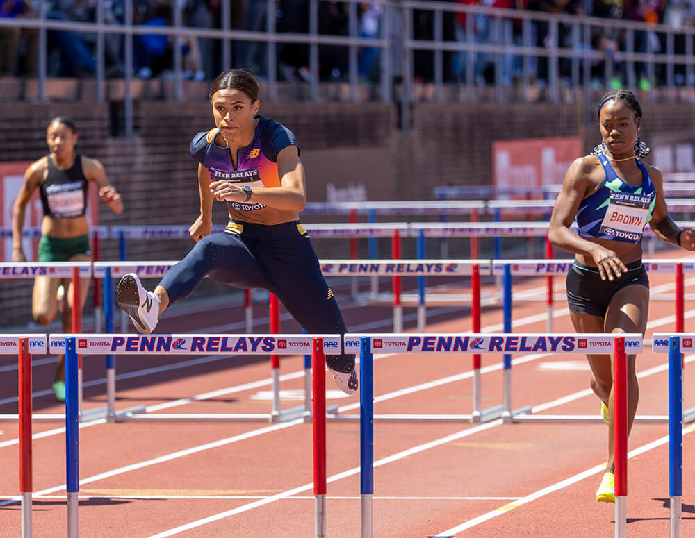 Athletes are shown jumping over hurdles on a track.