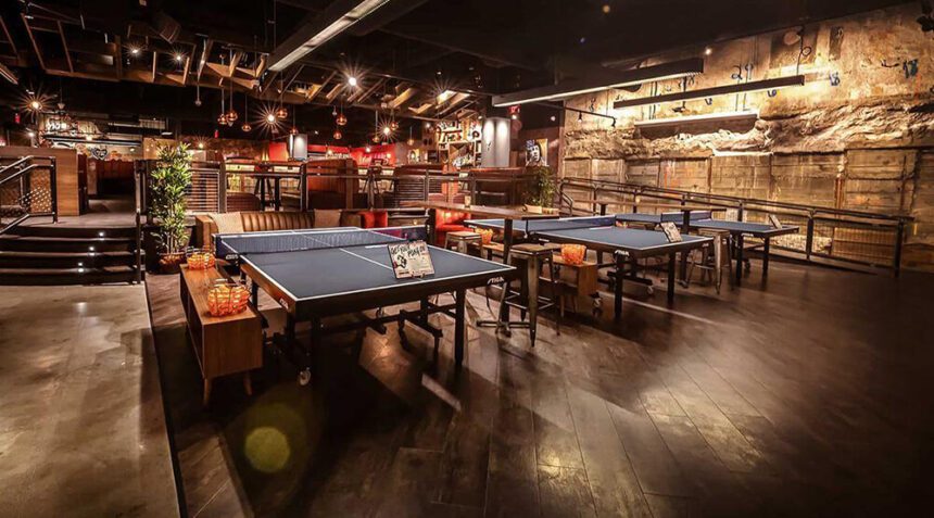 An industrial interior space with brick walls, dark wood floors, and ping-pong tables.