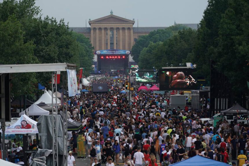 Hundreds of people are shown on the Benjamin Franklin Parkway. The Philadelphia Museum of Art is in the center. There is a large stage set up in front of the museum. Tents are set up along the Parkway.