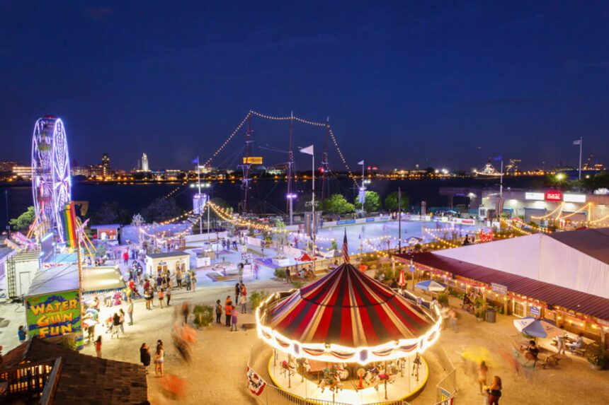 A dark blue nighttime sky is overhead. Below, a roller skating rink by river, a Ferris Wheel, a carousel and arcade games fill an outdoor space in a carnival-like atmosphere. People are shown enjoying the festivities.