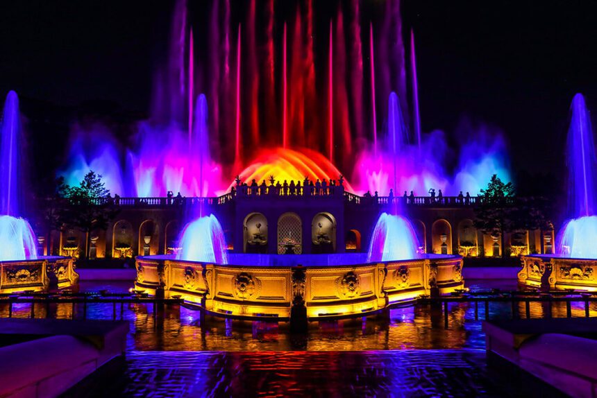 Bright colorful blue, purple, yellow, orange, and red lights illuminate a large fountain at Longwood Gardens.