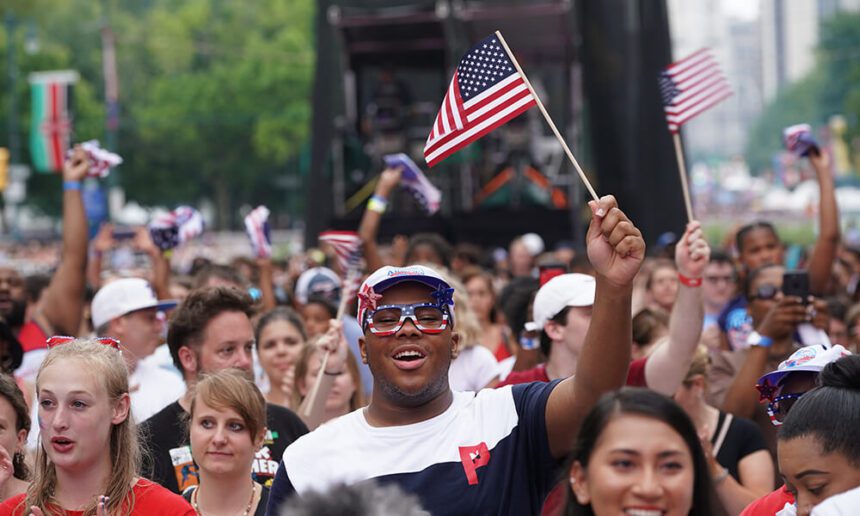 A person holds up an American flag in a crowd at the Wawa Welcome American Parkway concert.