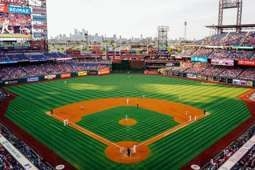 A baseball diamond is in the center. Packed stands with fans surround the field. The Philadelphia skyline is in the distance.