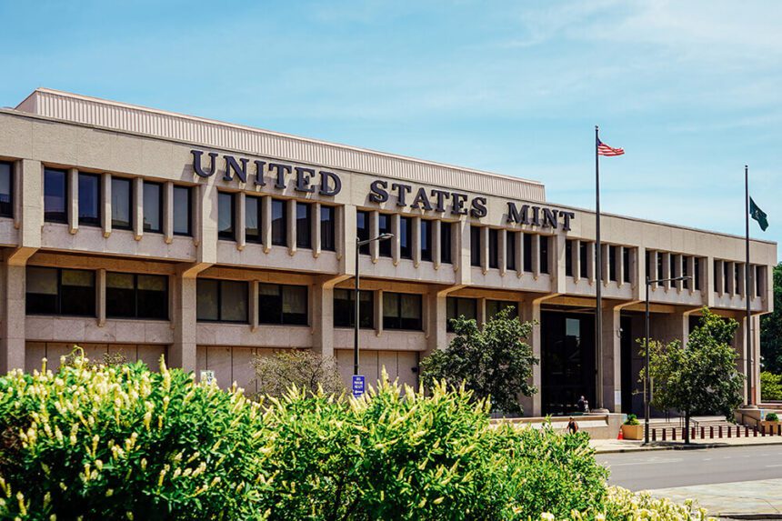 A large building is shown. Across the top, it reads UNITED STATES MINT. There is an American flag waving in the wind on top of a flag pole. There are green bushes in front.