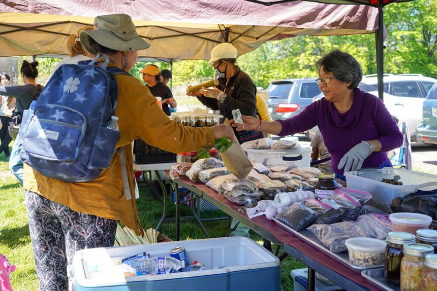 Two women exchange money over a table of food and goods at an outdoor farmers market in Philadelphia.