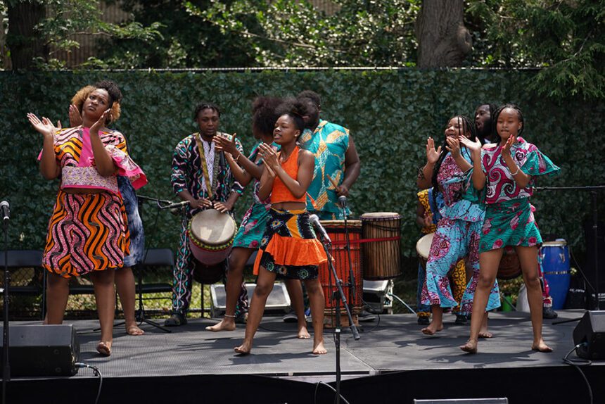 Young women dressed in brightly colored outfits are shown on a stage, performing with a band behind them. The show is a part of Juneteenth celebrations in Philadelphia.