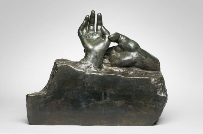 A bronze sculpture of two human hands is shown in front of a white backdrop.