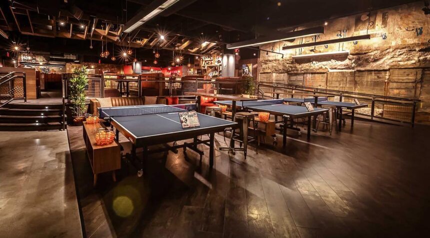 An industrial interior space with brick walls, dark wood floors, and ping-pong tables. 