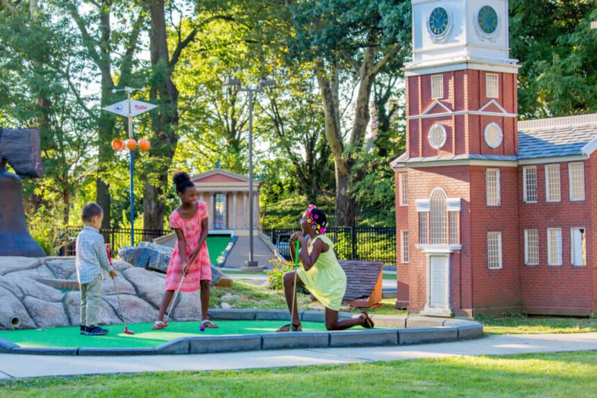 Three children play mini golf.