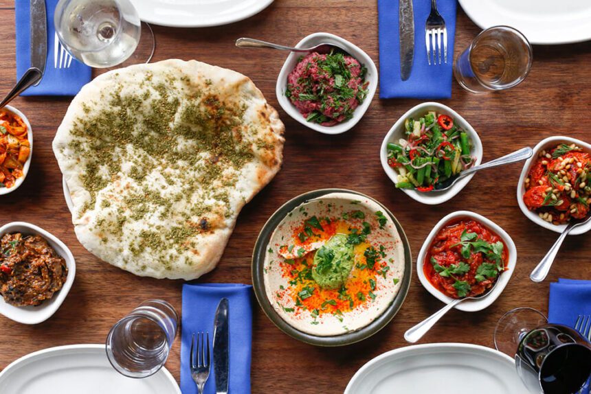 A table full of Mediterranean dishes, including hummus, pita, and various colorful veggies.
