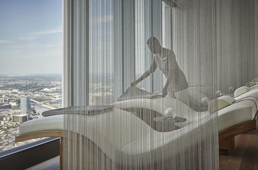 Behind a beaded curtain, a spa employee arranged towels on luxury spa chair looking out on an expansive view of the city.