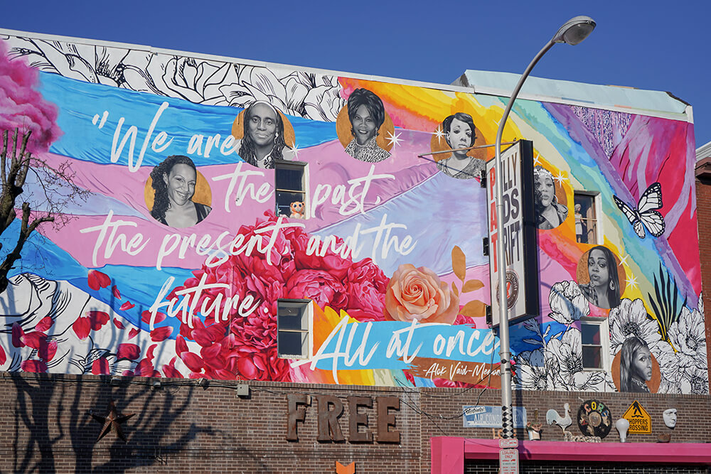 A colorful mural shows multiple women's faces with the quote: 