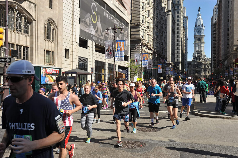 Runners are shown running down a street with Philadelphia's City Hall behind them during the annual Broad Street Run.