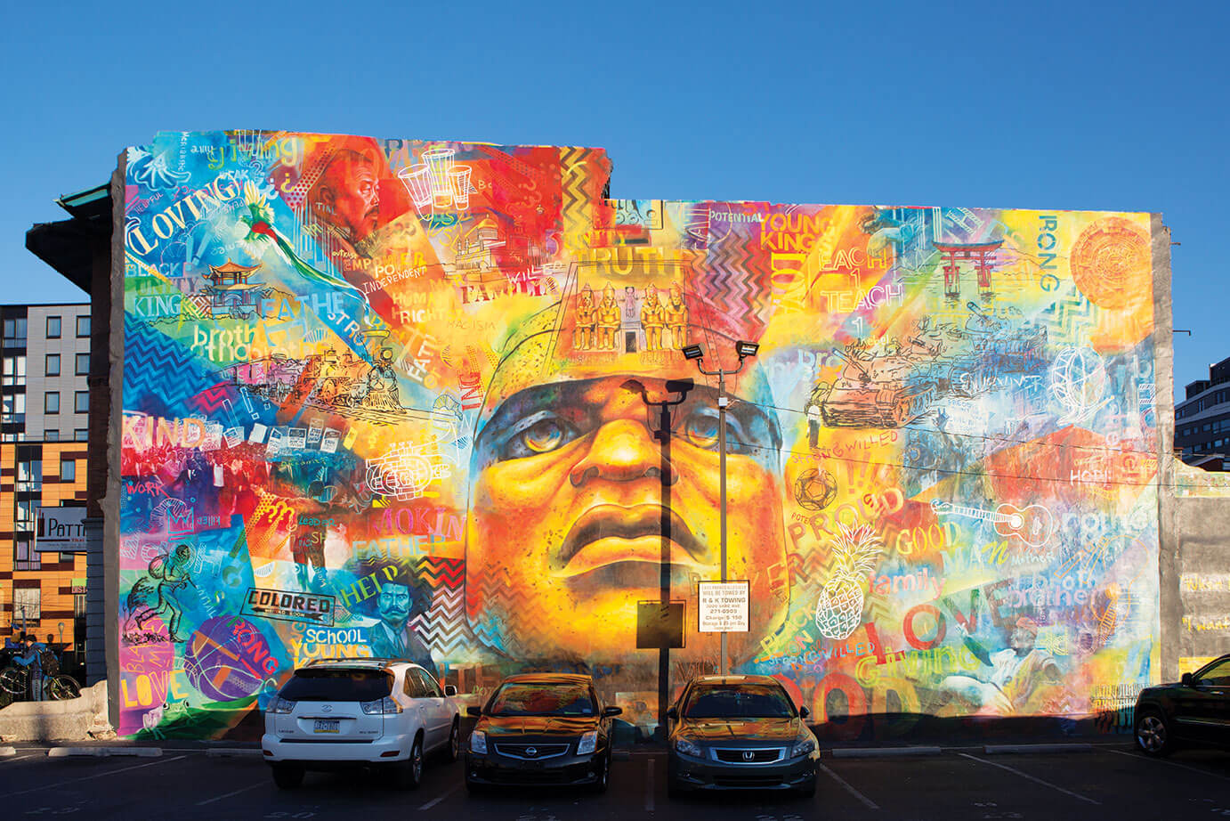 Colorful mural on the side of a building, face is in the middle, with what appear to be rays of light shining from it with other images
