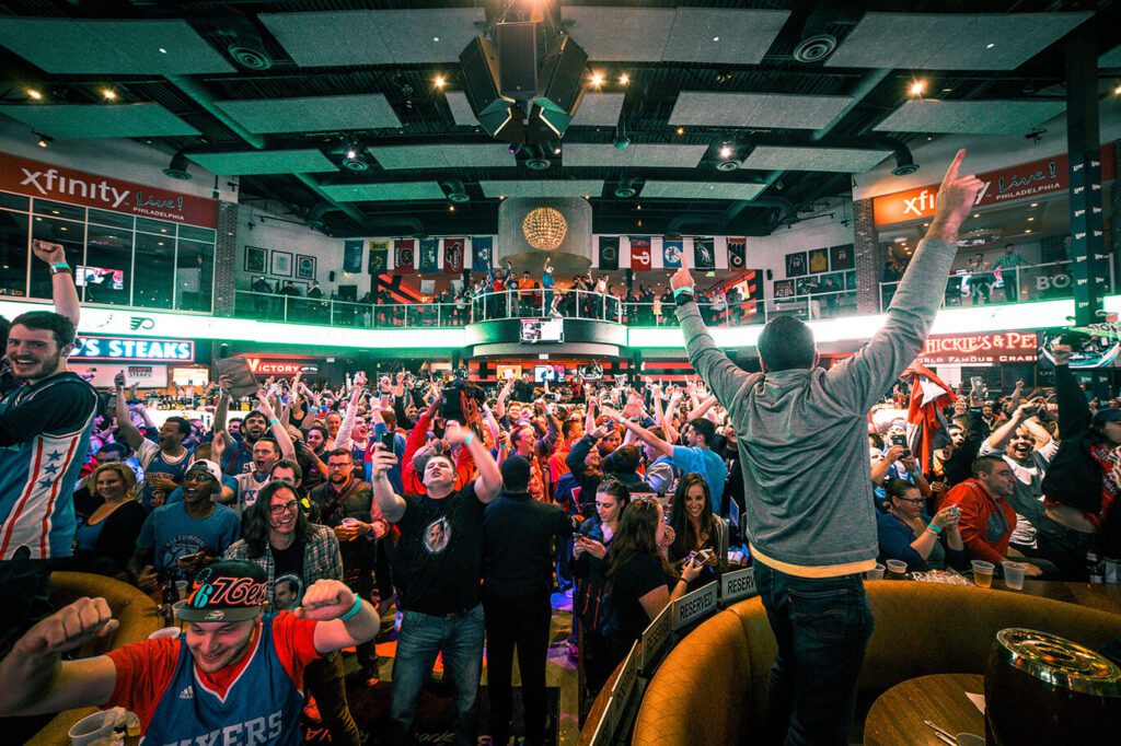 A large crowd of sports fans inside a bar cheer for their team.