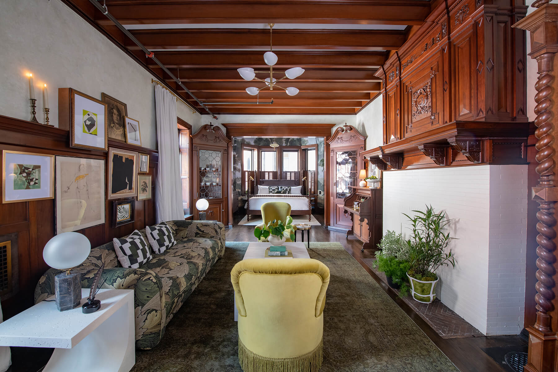 An indoor living space is shown. A yellow chair is shown in the middle of a room. There is a couch to the left. There are plants and various items of decor spread throughout the inviting space.