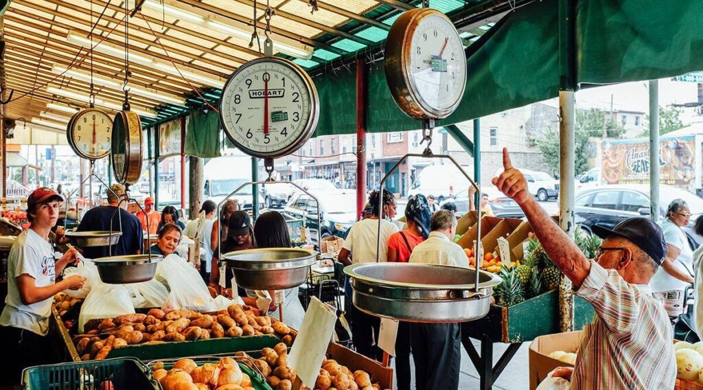 Several shoppers visit the crowded Italian Market and buy various fruits and vegetables from the stands.