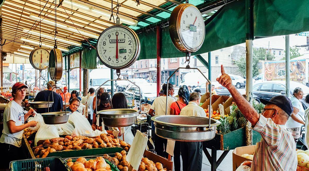 Several shoppers visit the crowded Italian Market and buy various fruits and vegetables from the stands.