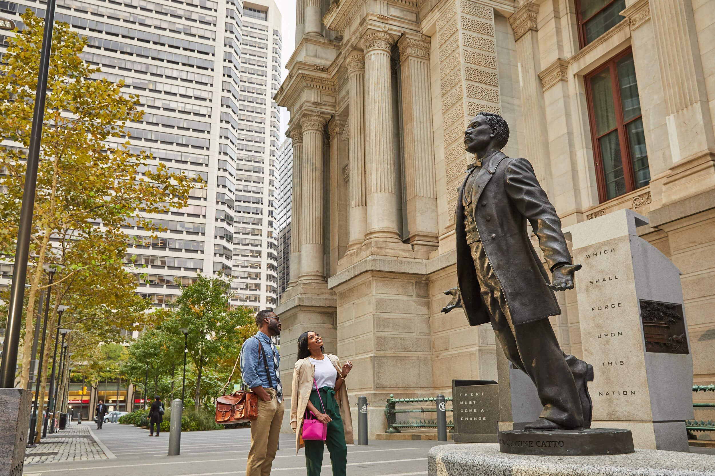 Two people, a man and a woman, looking up at the Octavius V. Catto sculpture outside of Philadelphia City Hall