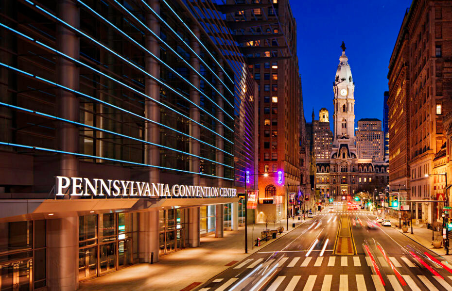 It is nighttime in the city. Philadelphia City Hall is shown off to the right at the end of the street. The Pennsylvania Convention Center is off to the left.