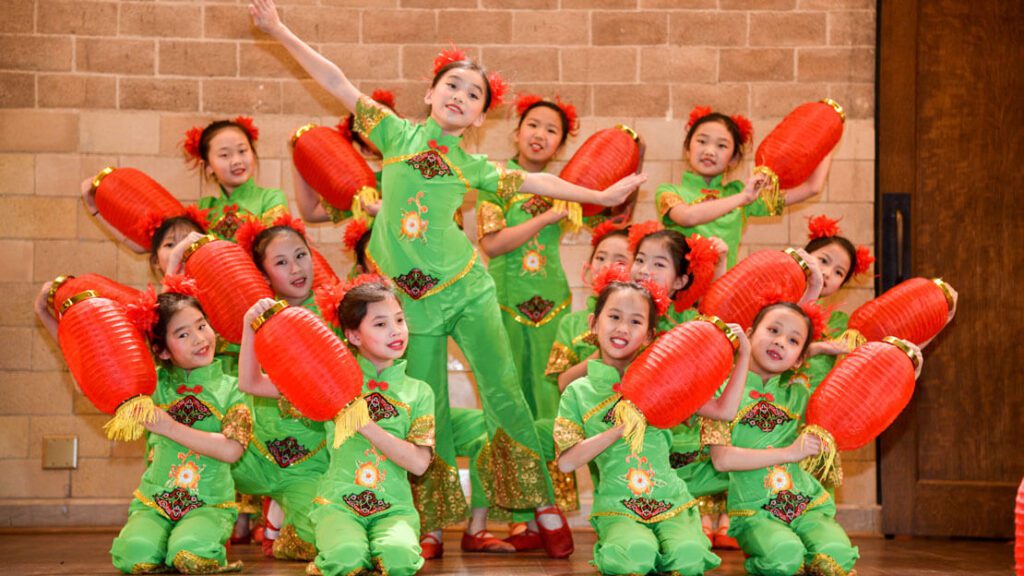 Children in bright green and orange costumes perform with lanterns in celebration of the Lunar New Year
