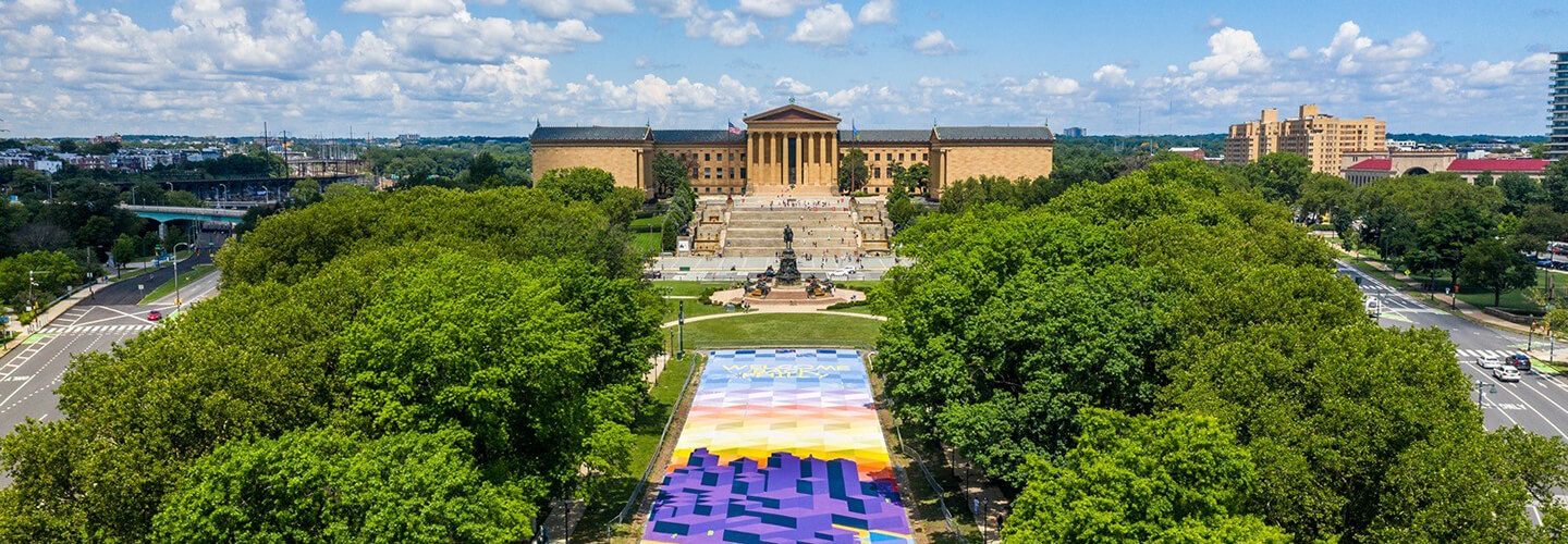 A large neo-classical building behind a fountain on a parkway full of lush green trees.