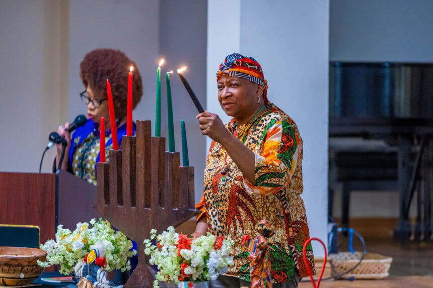 A woman stands in a colorful outfit lighting red and green candles in celebration of Kwanzaa at the African American Museum in Philadelphia.