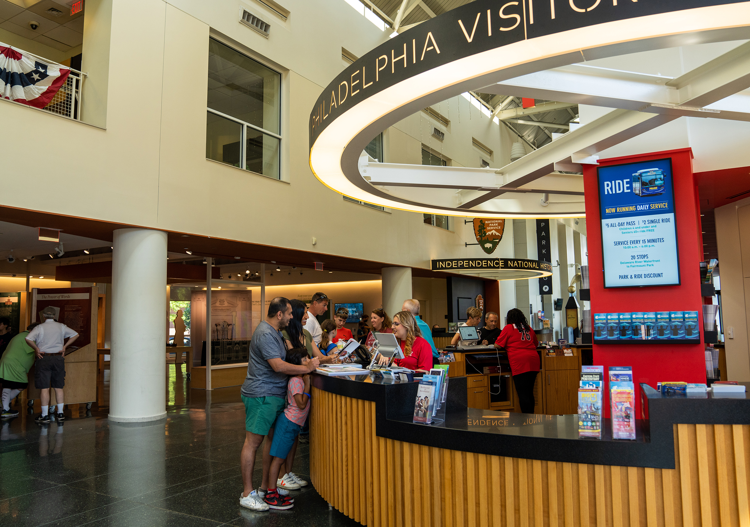 Inside a visitor's center a family speaks to a person at the front desk while reviewing a visitors guide.