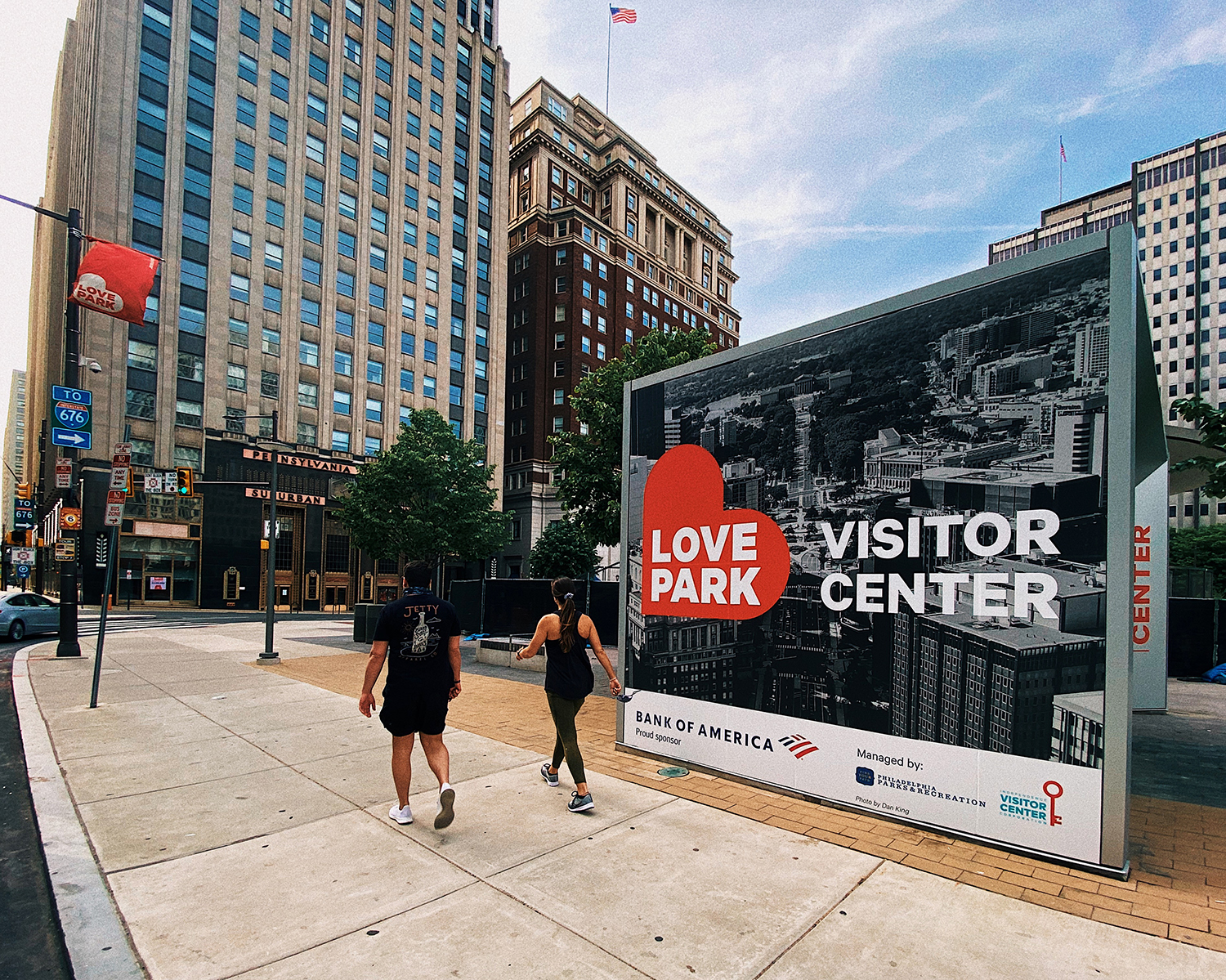 Two pedestrians walk past a glass building with the name 