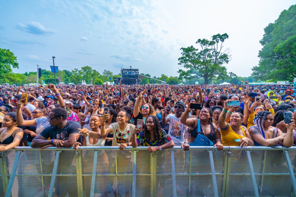 A crowd at a concert barricade enjoying The Roots Picnic outside.