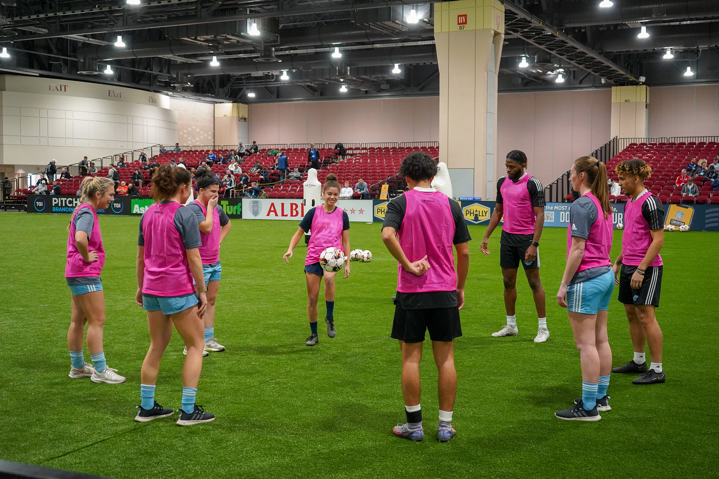 A group of teenagers kick around a soccer ball on an indoor field.