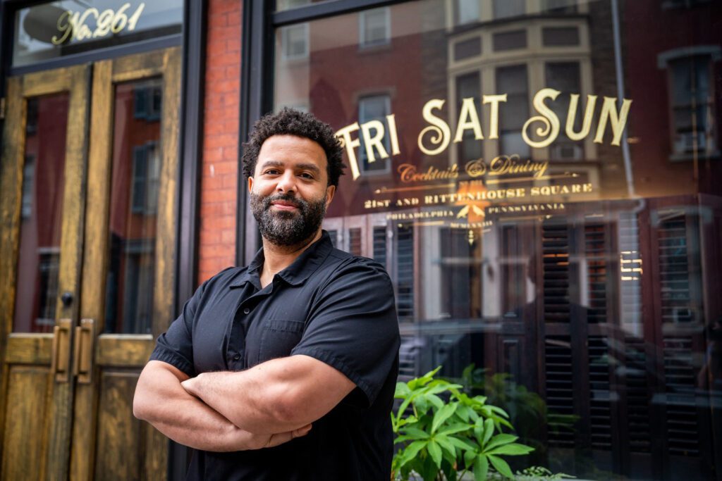A chef crosses his arms outside his restaurant, Fri Sat Sun.