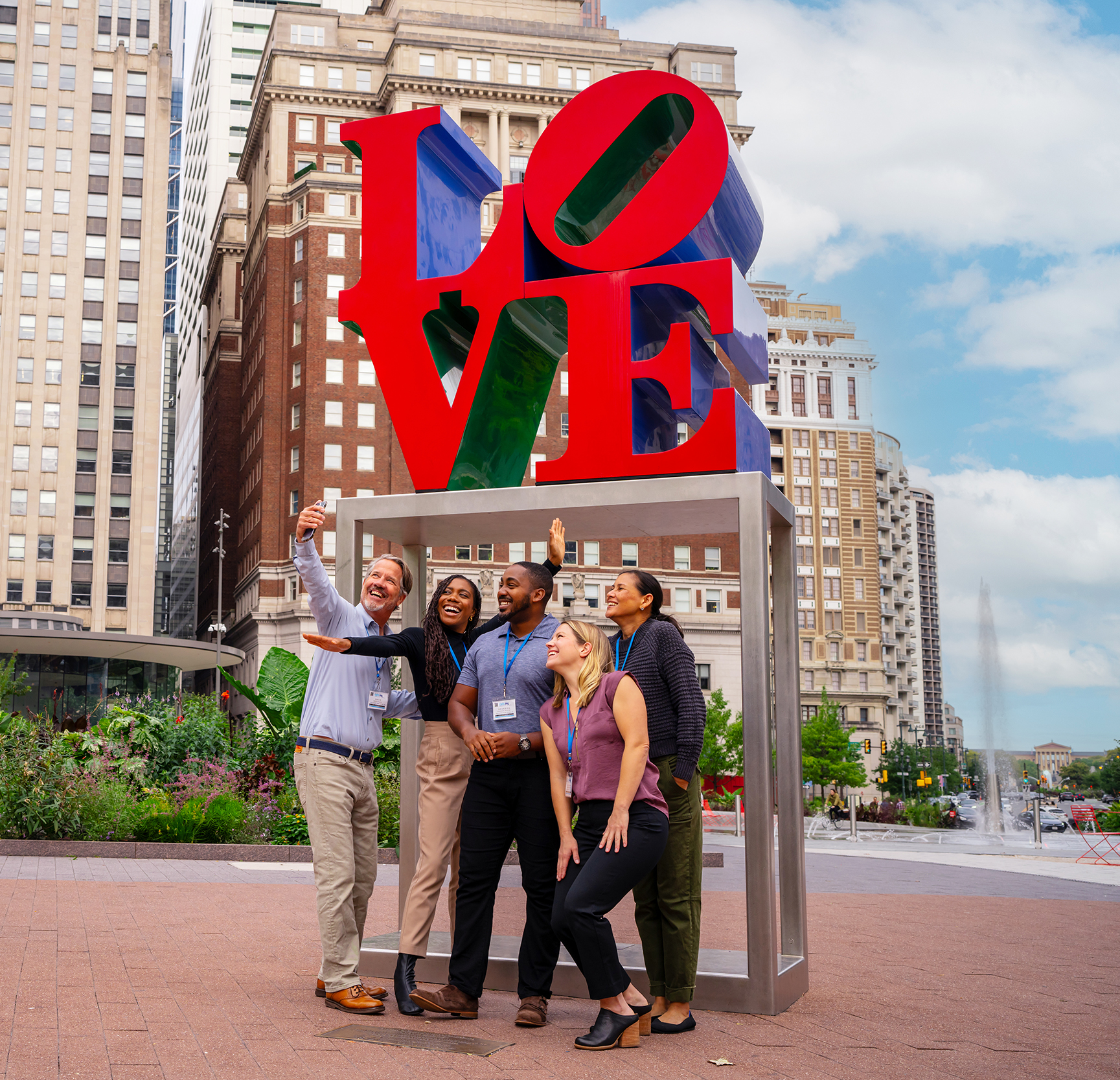 A group of people wearing convention badges pose for a selfie in front of the LOVE statue.