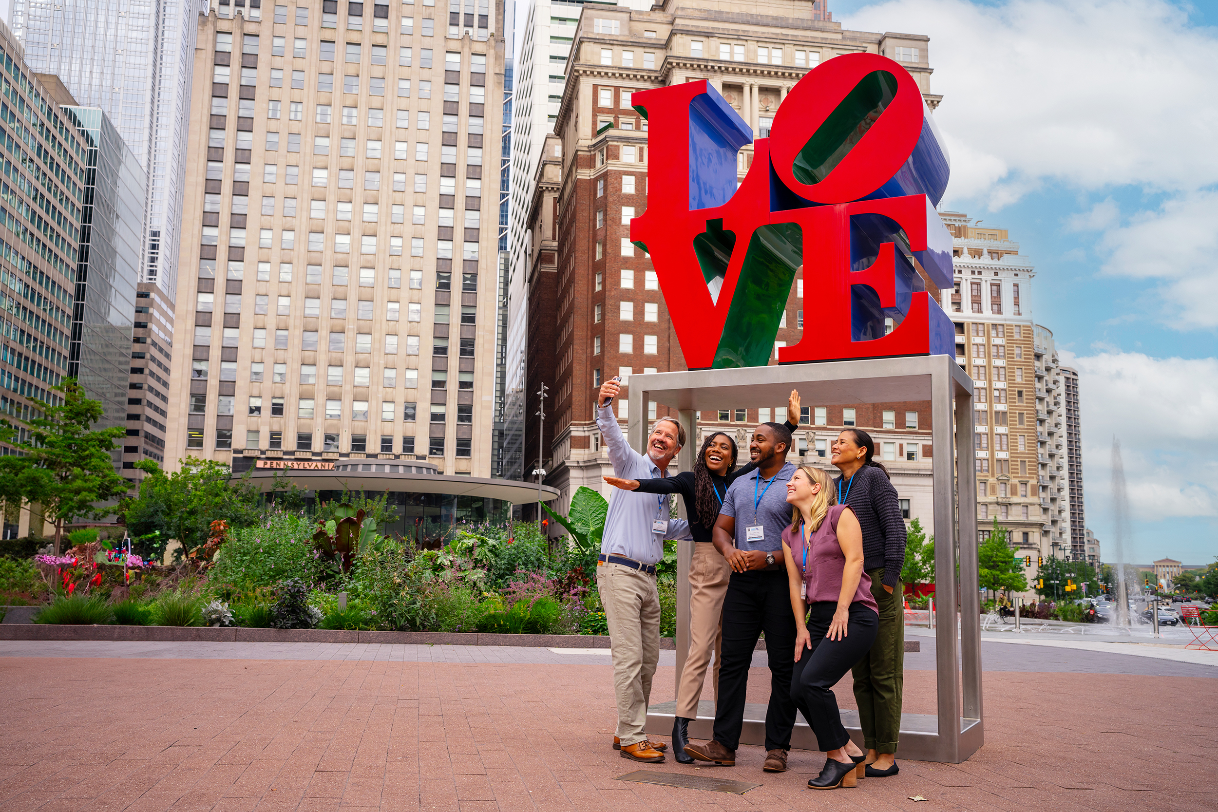 A group of people wearing convention badges pose for a selfie in front of the LOVE statue.