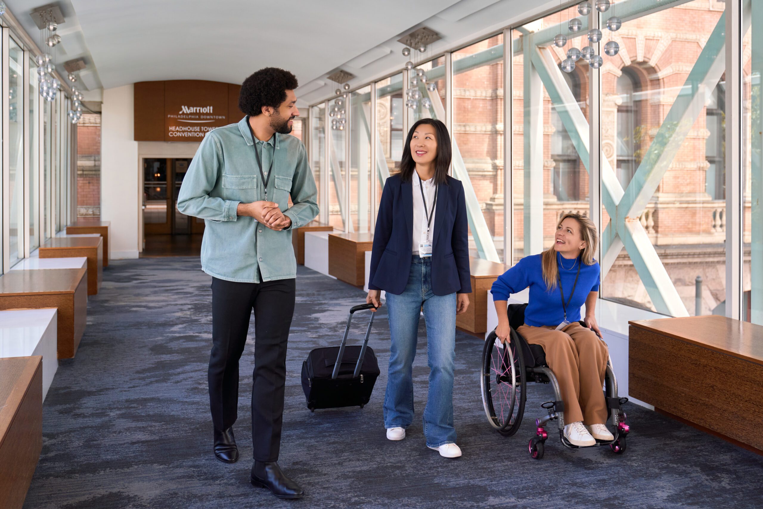 A man, a woman, and a woman in a wheelchair in the skybridge linking the Philadelphia Downtown Marriott and the Pennsylvanian Convention Center.