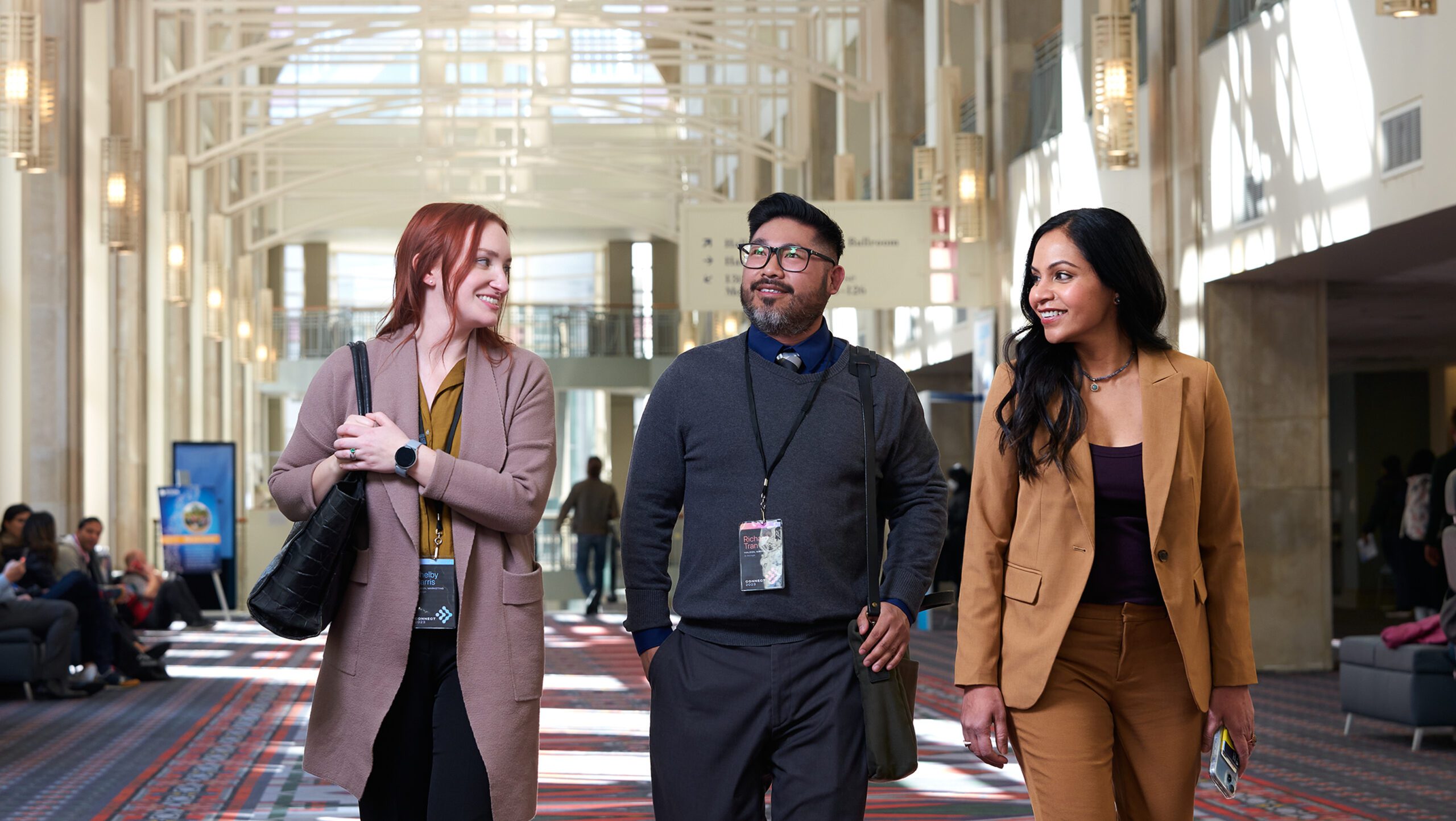 Three people walk down a hallway chatting with each other.