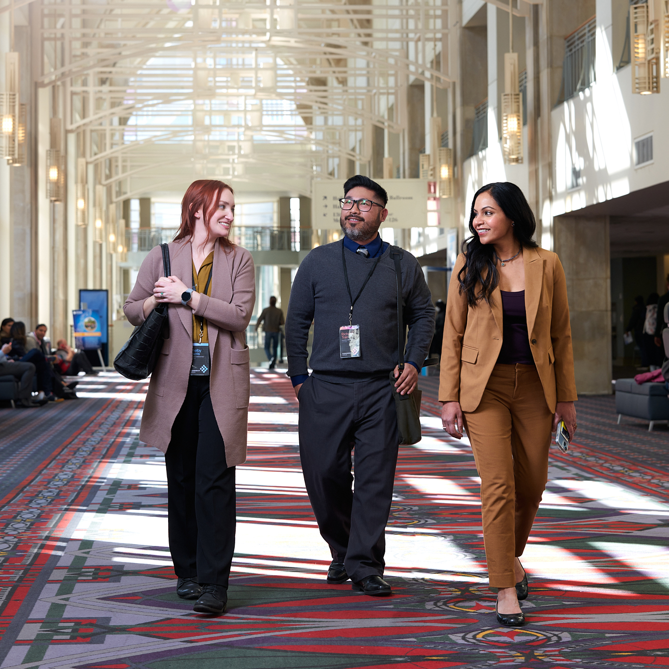 Three people walk down a hallway chatting with each other.