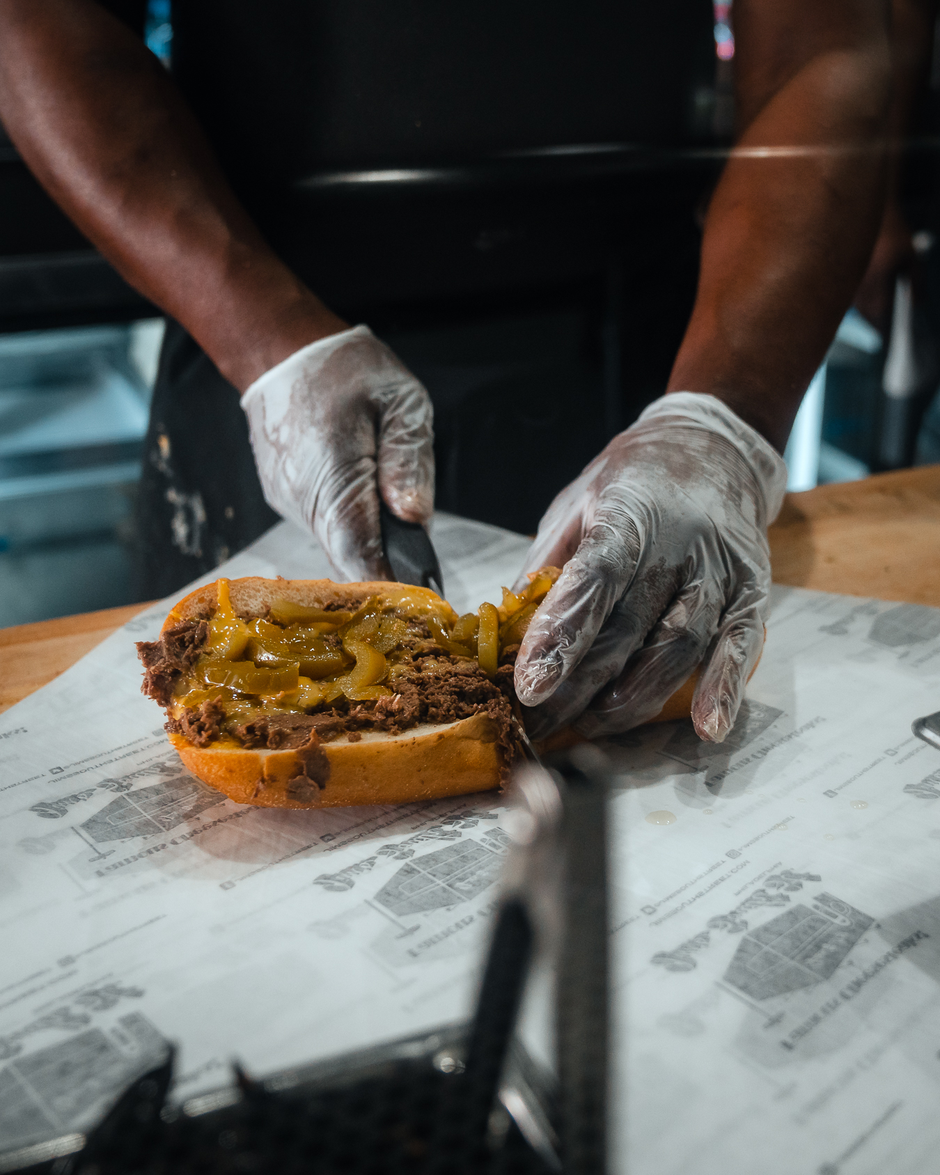 A cheesesteak being cut in the center over Jim's Steaks paper/
