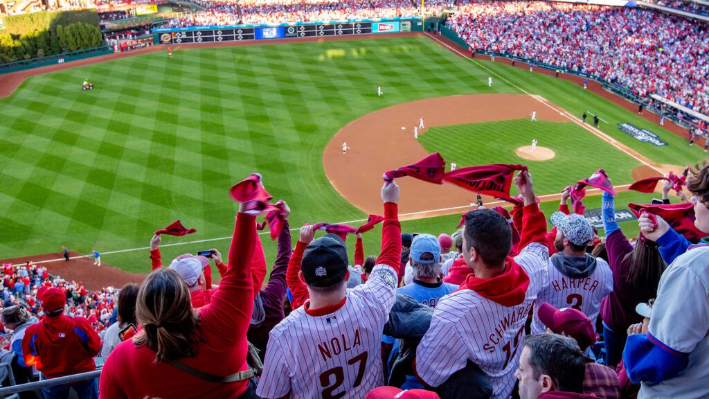 A stadium full of Phillies fans wave their rally towels excitedly while watching a baseball game.