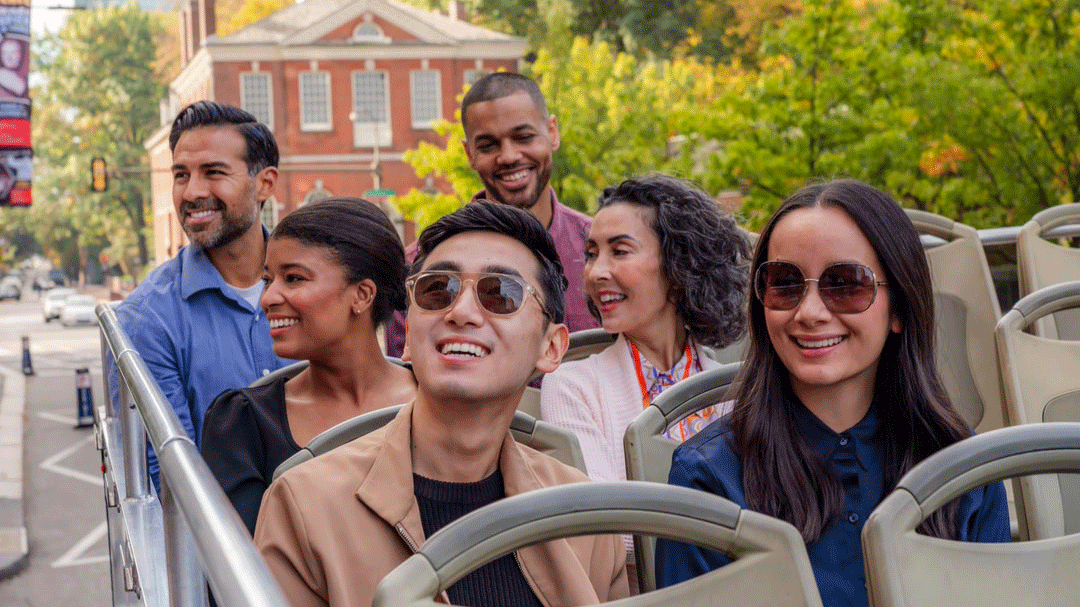 A group of people site seeing in rooftop seats on a tour bus in Philadelphia.