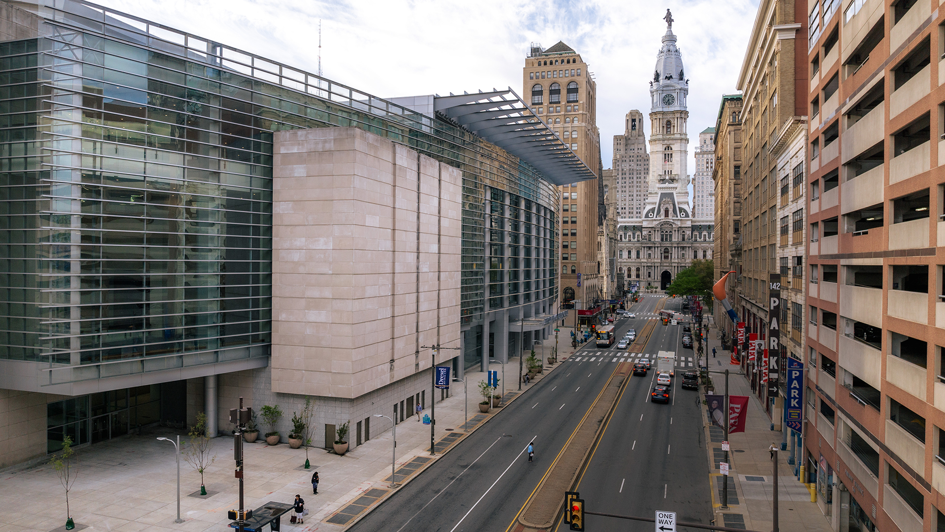 Outside of Pennsylvania Convention Center, a tree is in the bottom left hand corner of the frame, street is shown with a car driving toward City hall in the distance