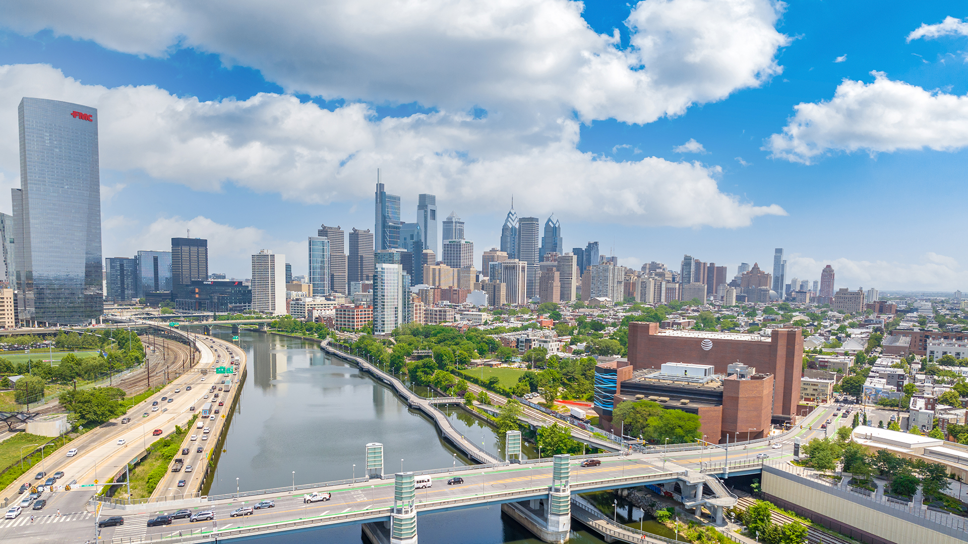 A view of Philadelphia's skyline from the south, over a river with a bridge. The skyline sits to the east of the river.