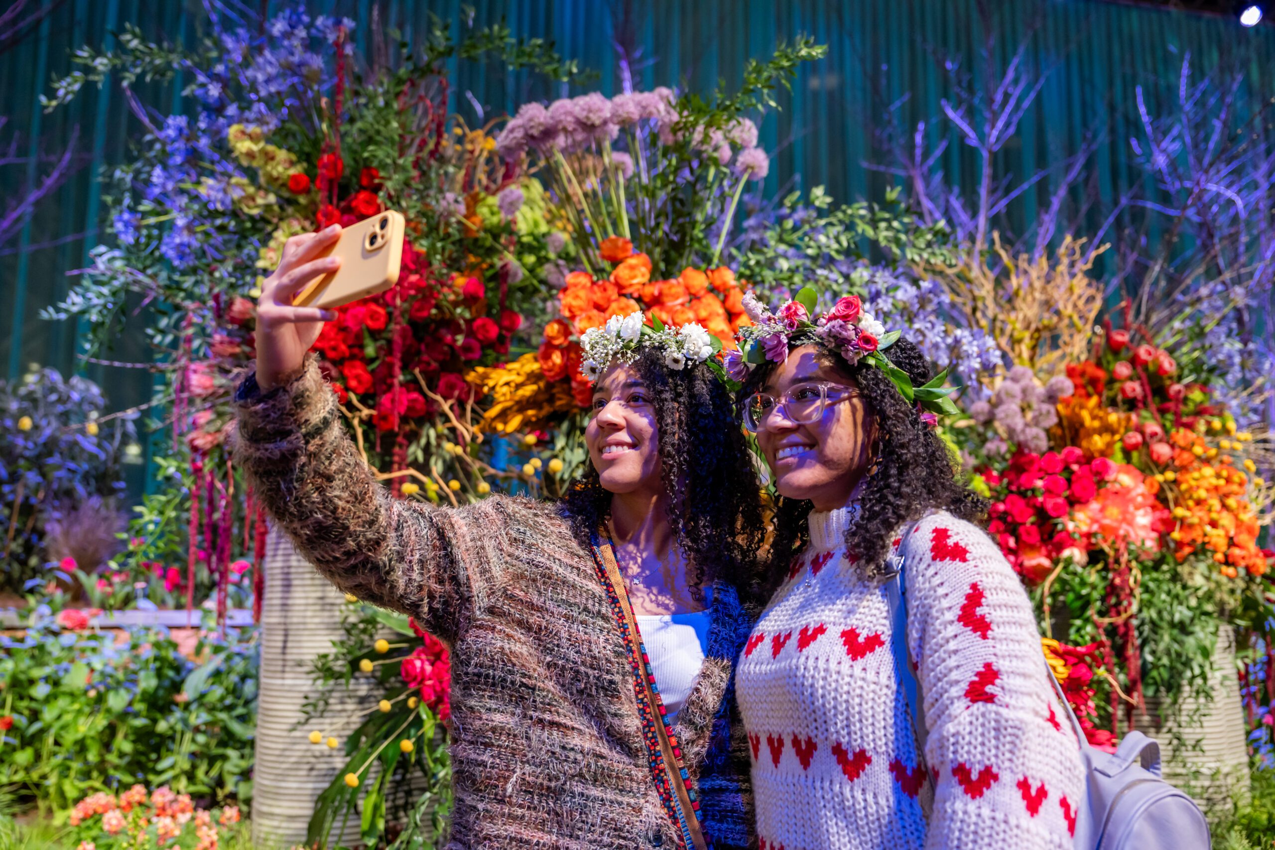 Two women take a selfie in front of a flower display at the PHS Flower Show.